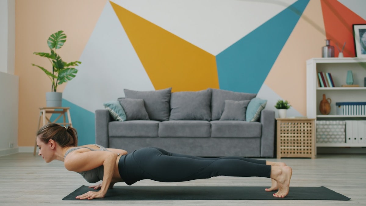 Athletic young lady is exercising at home in plank position then doing yoga downward dog asana stretching body on mat. Millennials and sports concept.